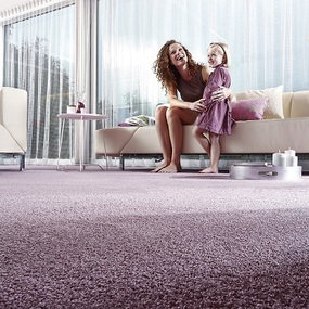 Frau und Kind sitzen lachend auf Sofa im modernen Wohnzimmer mit flauschigem Teppichboden.